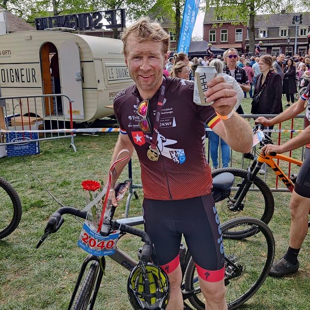 Picture taken at an event, depicting a smiling cyclist next to his bike with a Thrive can in his hand